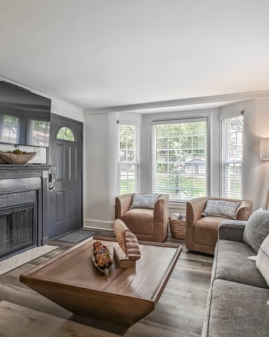 Open-plan living room with black sofa, brown accent chair, TV on blue media console, and glass doors opening to balcony.